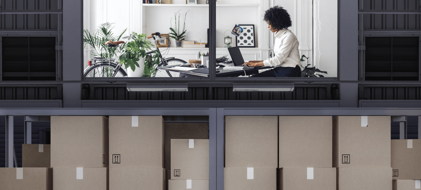 Senhora a trabalhar no seu computador, por cima de um armazém de encomendas