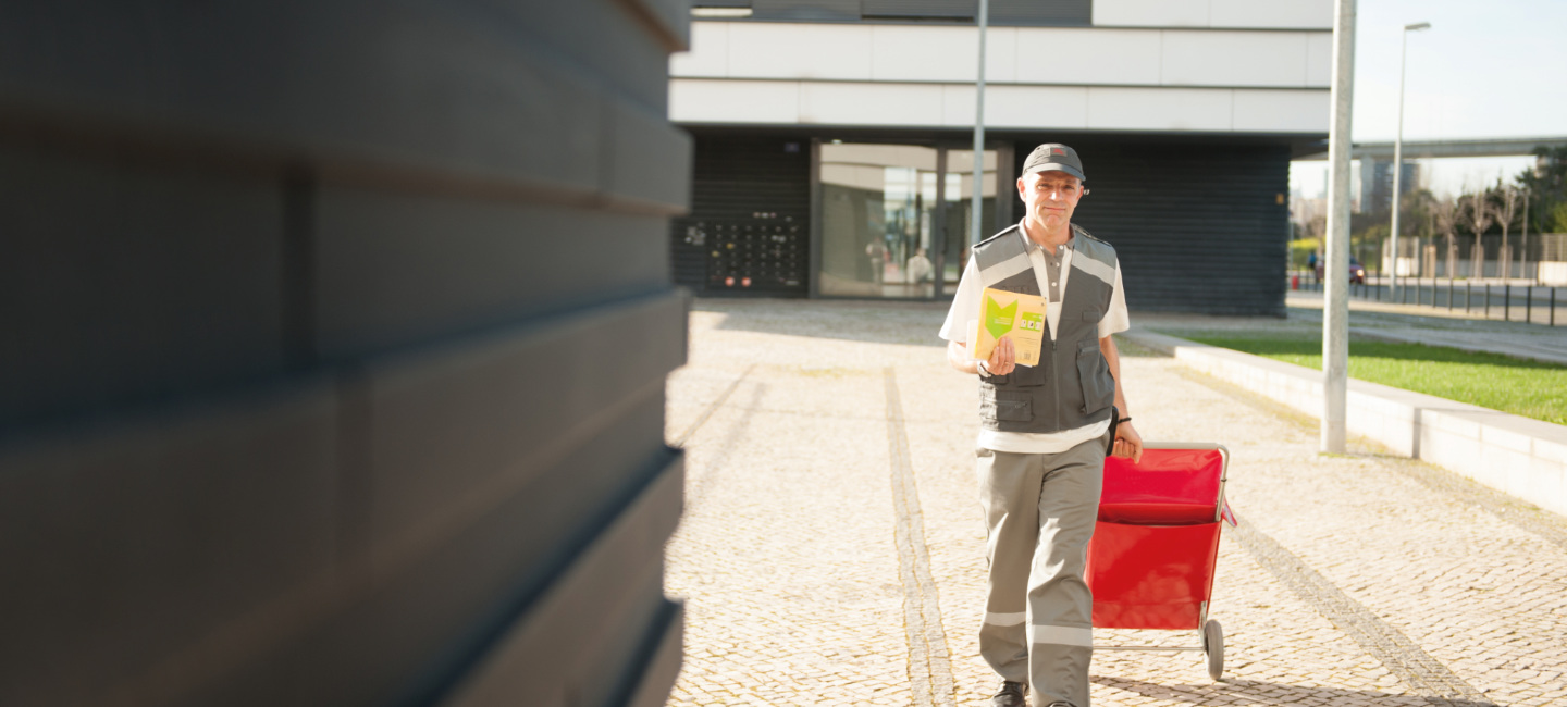 Carteiro a distribuir correio, puxando o seu carrinho de mão.