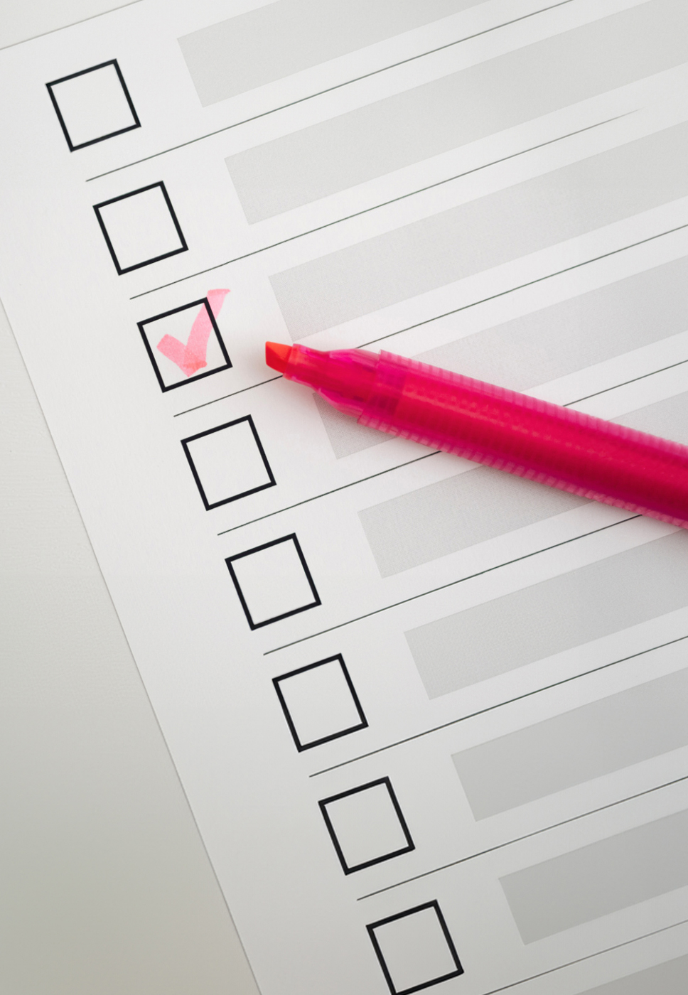 A imagem mostra uma lista de verificação com várias caixas de seleção vazias. Uma das caixas de seleção está marcada com um visto rosa, e há uma caneta marca-texto rosa ao lado, indicando que o visto foi feito com essa caneta. A imagem representa o conceito de completar tarefas ou itens em uma lista.