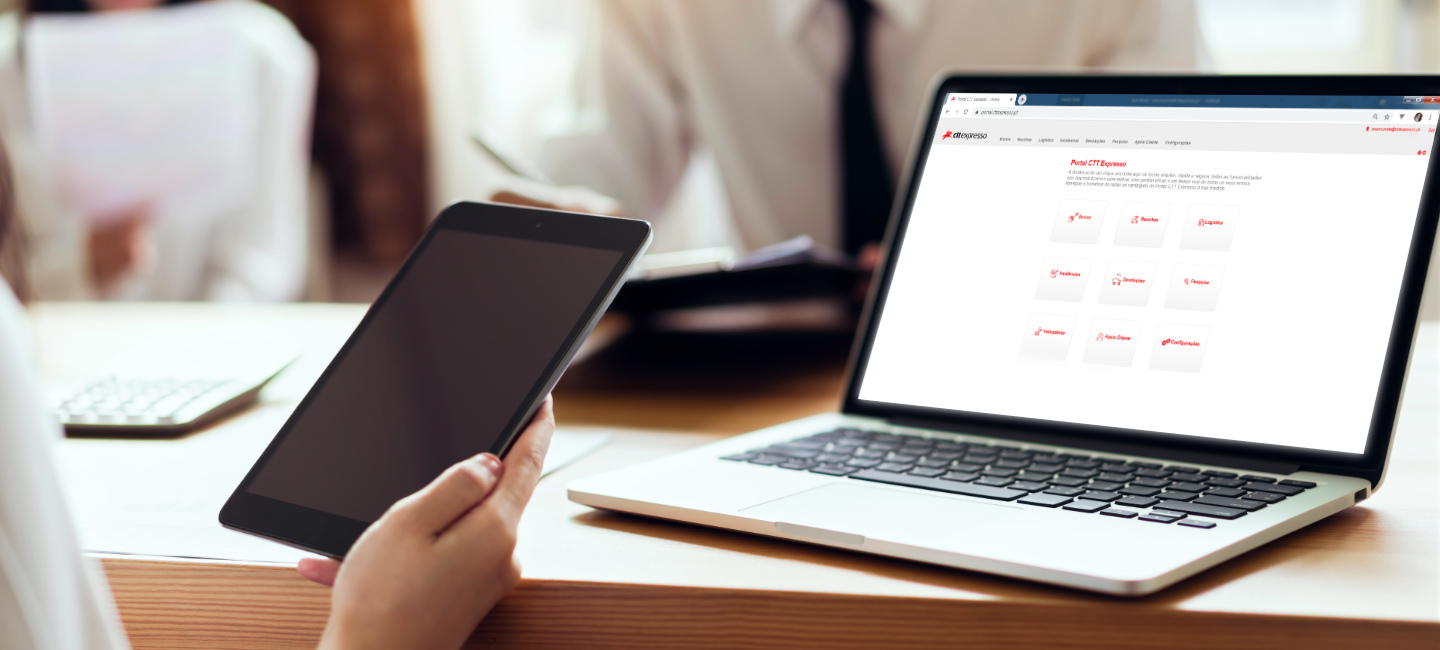 Pessoa segura um tablet com um portátil à sua frente.