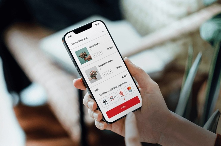 Telemóvel na mão de uma pessoa. No ecrã estão várias opções de pagamento: MBWay, Payshop, Multibanco e VISA.